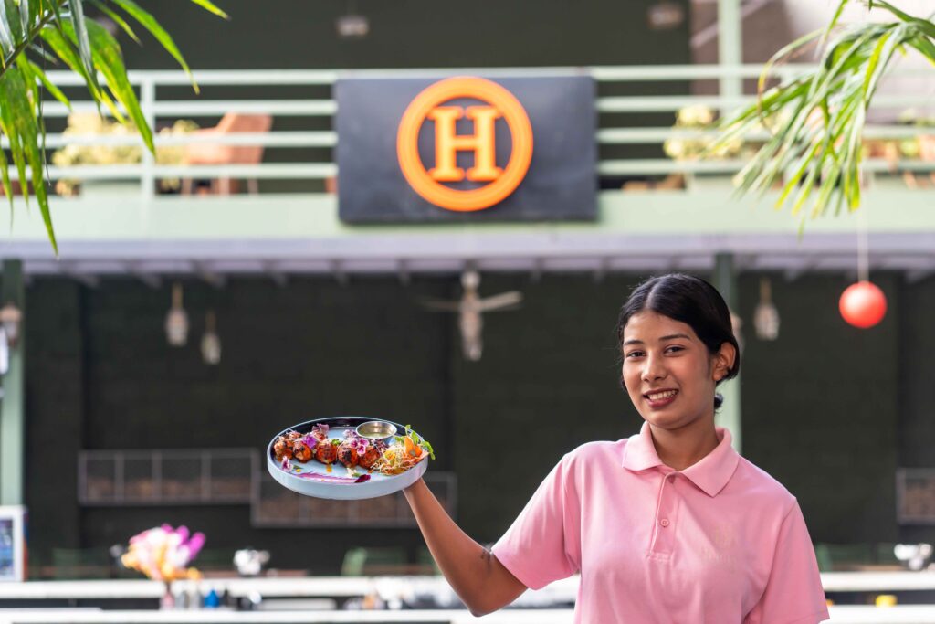 Waitress in pink uniform holding a dish of colorful food skewers at a cafe.